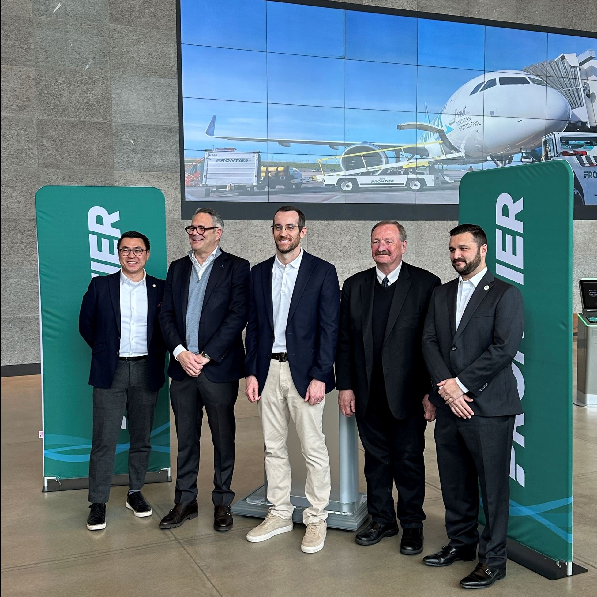 Five men in dark suits and ties announce new airline service from Frontier Airlines.