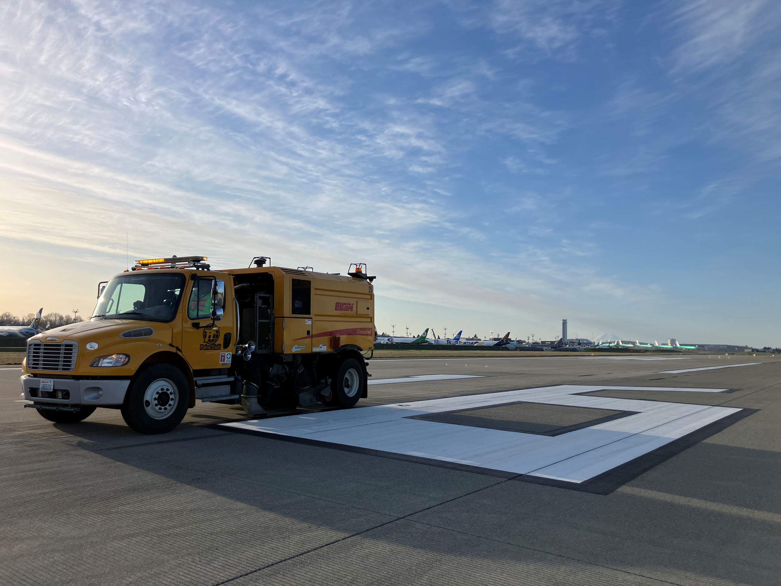 Bright yellow street sweeper cleans Runway 16R at Paine Field against a bright blue sky